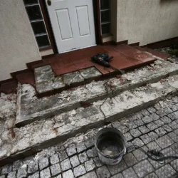 Schody wejściowe z częściowo skutymi płytkami i narzędziami na górnym podeście.
