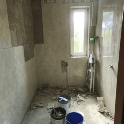 Łazienka w Piasecznie podczas skuwania płytek, z gruzem na podłodze i drabiną przy oknie.