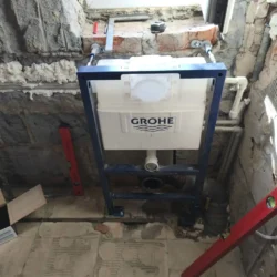 Stelaż WC z podłączonymi rurami na odsłoniętej ścianie pod oknem.