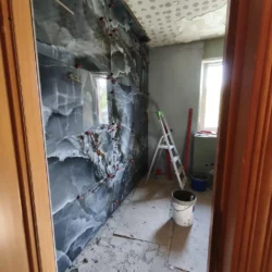 Układanie ciemnych płytek z kamiennym wzorem wokół okna w łazience.
