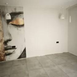 Ściana z fototapetą przedstawiającą twarz kobiety oraz dwiema białymi lampami wiszącymi